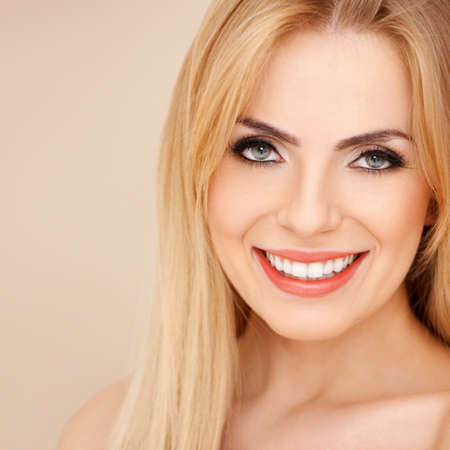 Close-up of pretty smiling blond girl with exposed shoulders, over muted backgroundの写真素材