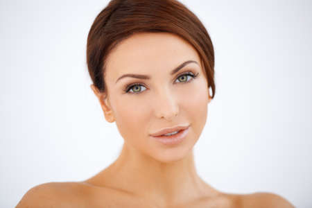 Beautiful serene woman with lovely smooth skin and a gentle look posing against a white background with bare shouldersの写真素材