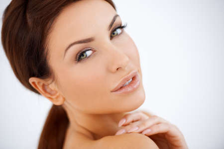 Beautiful natural sensual woman posing looking over her shoulder at the camera with a seductive look, studio portrait with topless shouldersの写真素材