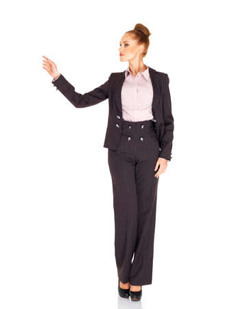 Tall elegant woman in a stylish slacksuit with her hair in a bun standing pointing her finger to the side towards blank copyspace isolated on whiteの写真素材
