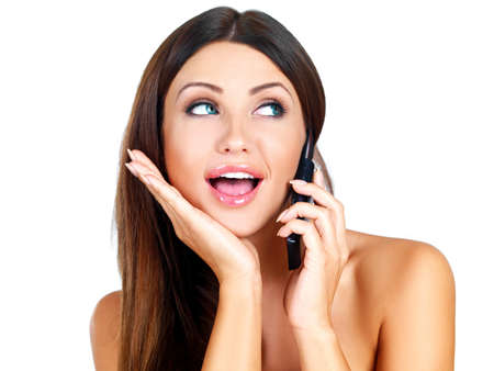 Attractive young woman standing gossiping on her mobile phone with her eyes raised looking to the side isolated on whiteの写真素材