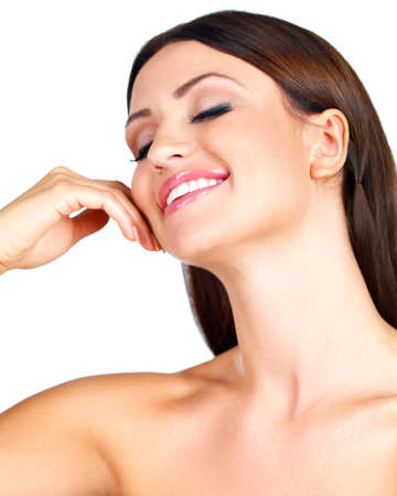 Beautiful young woman with bared shoulders tilting her head back caressing her cheek with her hand smiling in pleasure and bliss isolated on whiteの写真素材