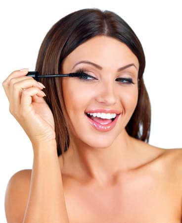 Head and shoulders beauty portrait of a happy  woman with a beautiful smile applying mascara with a brush to her long eye lashes isolated on whiteの写真素材