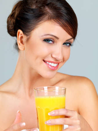 Smiling beautiful woman with bare shoulders drinking a large glass of freshly squeezed orange juiceの写真素材