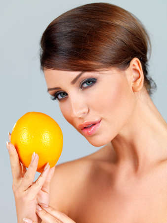 Sensual beautiful woman holding up a ripe fresh orange in her hand on a grey studio backgroundの写真素材