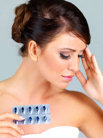 Beautiful young woman with a bad headache holding her hand to her forehead and a blister pack of pills in the otherの写真素材