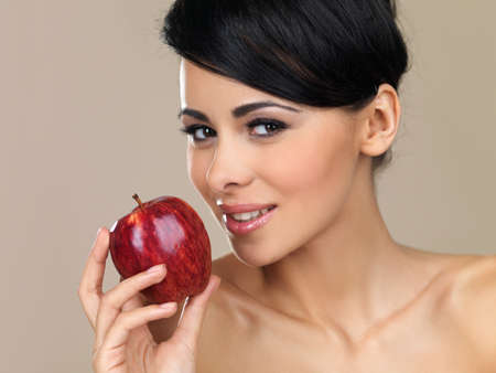 Beautiful young brunette woman with a large juicy ripe red apple in her hand on a beige studio backgroundの写真素材