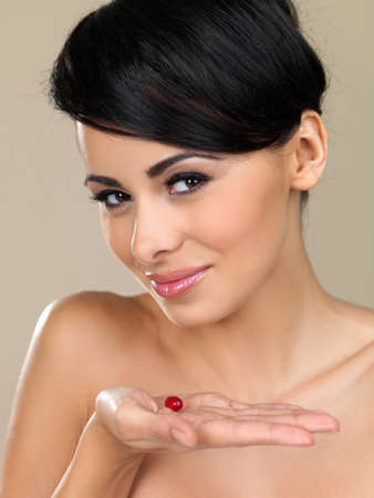 Beautiful bare shouldered woman with a lovely smile holding a capsule in her hand isolated on beigeの写真素材