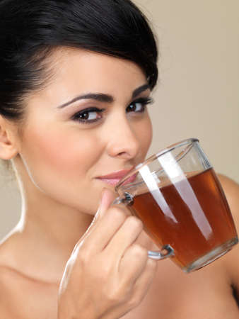 Closeup cropped portrait of an attractive woman drinking tea from a glass mug while glancing across at the cameraの写真素材