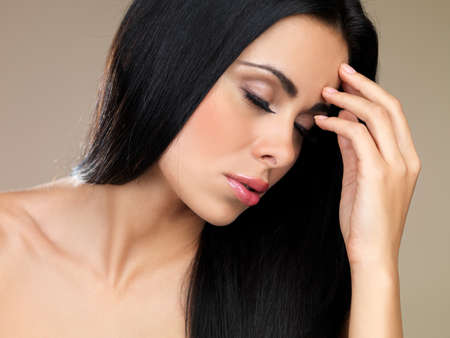 Beautiful sensual brunette woman with her eyes closed and her head tilted forwards with her hand to her foreheadの写真素材