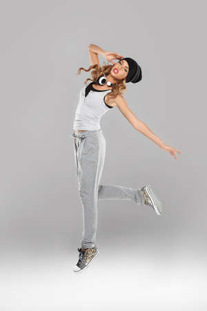 High-spirited beautiful young woman in casual clothes and trainers dancing and leaping in the air with a pair of music headphones slung around her neckの写真素材
