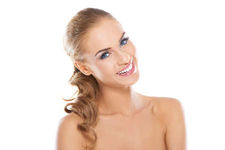 Smiling beautiful blonde woman with long curly hair posing with bared shoulders against a white backgroundの写真素材