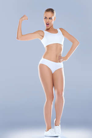Fun image of a shapely athletic woman in skimpy sportswear displaying her biceps which are unforunately rather underdevelopedの写真素材