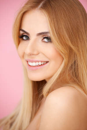 Portrait of a smiling blond girl on pink. Side viewの写真素材