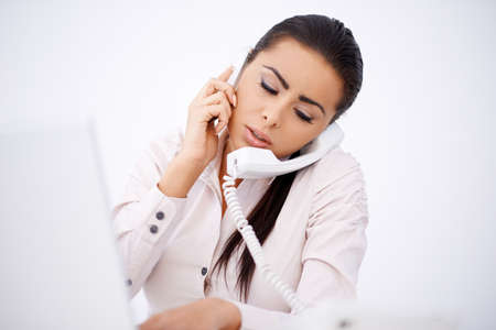 Overworked woman talking by cell phone and telephone simultaneouslyの写真素材