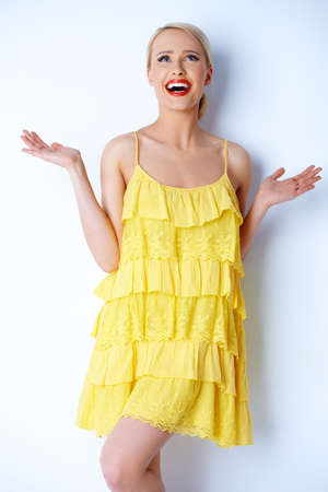 Hilarious blond woman posing over white background  she wearing yellow dressの写真素材