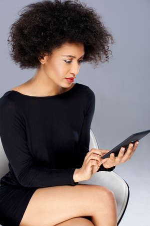 Vivacious chic African American woman with a wild afro hairdo posing in a glamorous see through pink top with a tablet tucked into the waistband of her slacks smiling at the cameraの写真素材