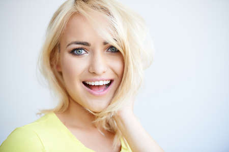 Laughing pretty young blond woman looking at the camera with a big smile  head and shoulders on grey with copyspaceの写真素材