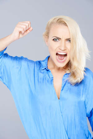 Temperamental attractive young blond woman raising her fist in anger and shouting at the camera in a fit of rageの写真素材