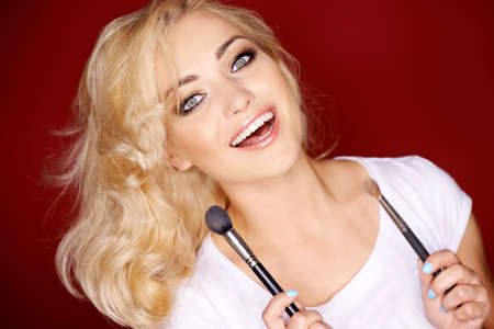 Beautiful sexy woman pouting seductively at the camera as she holding blusher with a large soft cosmetics brushの写真素材