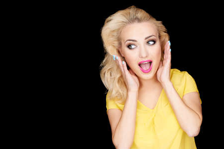 Beautiful young woman reacting in amazement holding her hands to her blond hair with her mouth open...
