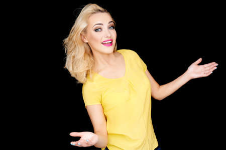 Young blond woman showing her ignorance smiling as she holds out her hands palm upwards to show she does not know or care  on blackの写真素材