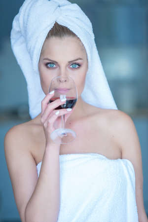 Young Woman in Bath Towel Sipping Glass of Red Wine and Staring at Cameraの写真素材