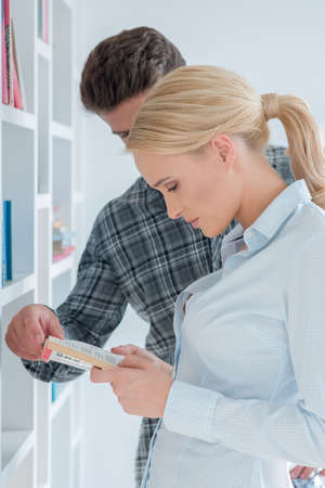 Close up Young Caucasian Couple Reading Book at White Home Mini Libraryの写真素材