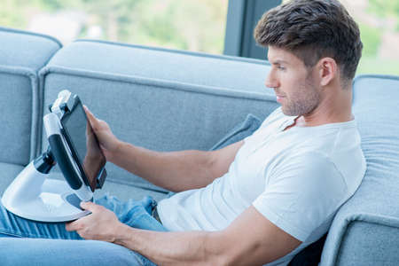 Young Handsome Man on Couch Playing His Gadgetの写真素材