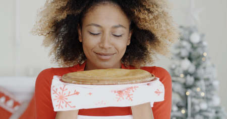 Young African woman with a freshly baked Christmas tart held in her hands smiling in pleasure as she savors the aromaの写真素材