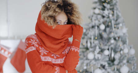 Fashionable young woman in a warm festive red woollen outfit standing in front of a decorated tree...