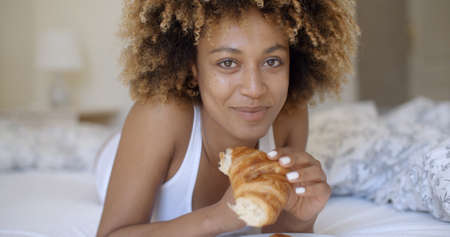 Pretty african american young woman enjoying a breakfast of fresh crisp croissantの写真素材