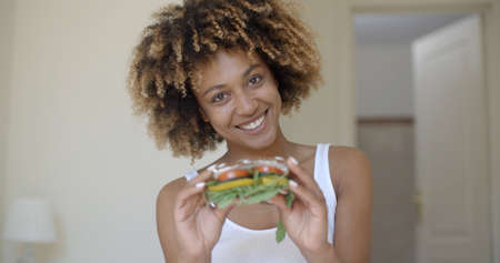 Young african american woman sits in bed and holding in hands healthy sandwichの写真素材