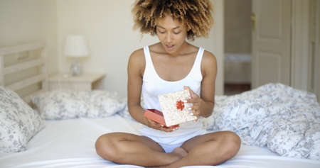 of a african-american woman open gift box at home in bedroomの写真素材