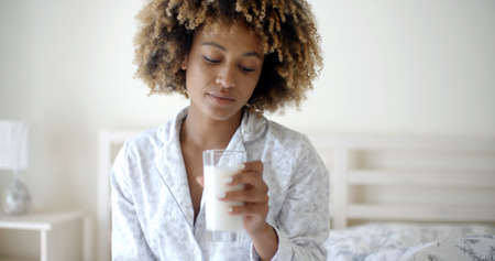 Relaxed woman drinking a milk while sitting on her bed at homeの写真素材