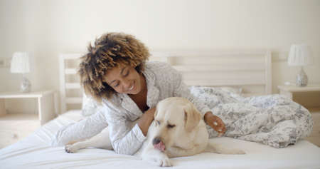 Young woman is holding a dog while laying on a bed in homeの写真素材