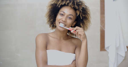 Black woman brushing her teeth and smiling in the bathroomの写真素材