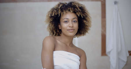 Woman covering her body with towel and smiling while standing in bathroomの写真素材