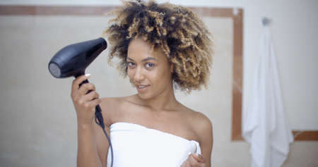 Portrait of young woman with fashion hairstyle holding hairdryer and drying her hairの写真素材