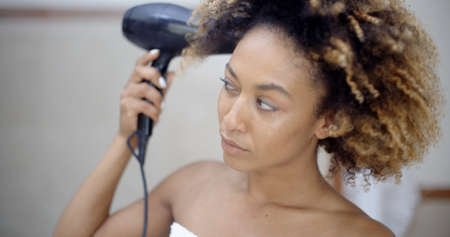 Beautiful afro haired girl blow drying her hair in the bath room.の写真素材