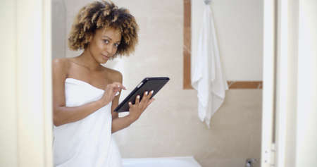 Girl in bath robe with touchpad networking in bathroomの写真素材