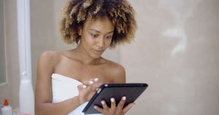 Girl in bath robe with touchpad networking in bathroomの写真素材