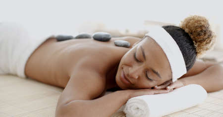 Beautiful ethnic client being treated with hot stone therapy at a luxury health spaの写真素材