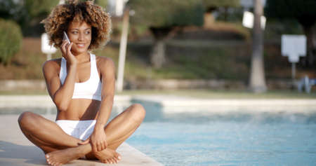 Woman talking on phone white relaxing near swimming poolの写真素材