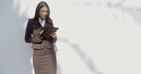 Business woman holding her digital tablet computer while standing against street wallの写真素材