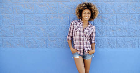 Young woman in summer clothes against blue stone wall flirting with cameraの写真素材