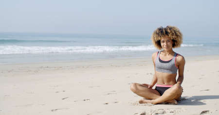 African american woman relaxing alone at the beach, sitting in lotus postureの写真素材