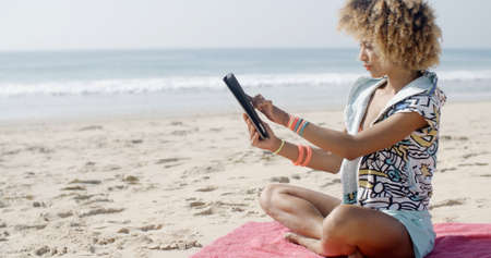 Carefree woman uses touchpad tablet technology on the beachの写真素材