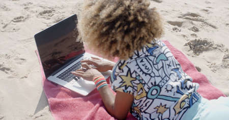 Young girl lying on the beach with a laptop and surfing in Internetの写真素材