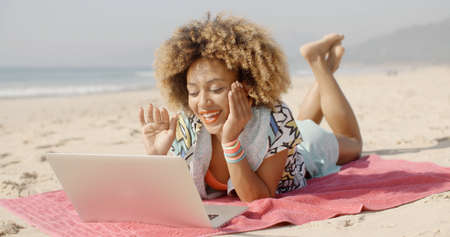 Woman relaxing at the beach while talking with her friend online.の写真素材